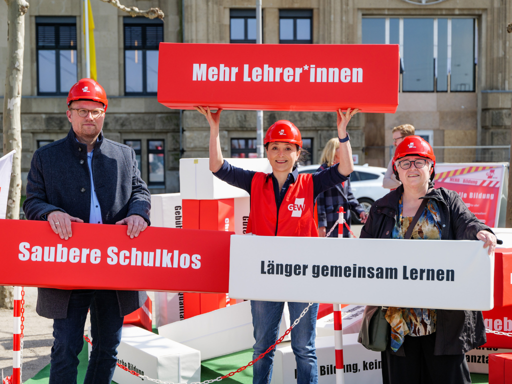 Jochen Ott (SPD), Ayla Çelik (Vorsitzende GEW NRW) und Sigrid Beer (Bündnis 90/ Die Grünen) halten Bausteine der Baustelle Bildung hoch. Auf ihnen steht: "Mehr Lehrer*innen", "Saubere Schulklos" und "Längeres gemeinsames Lernen"