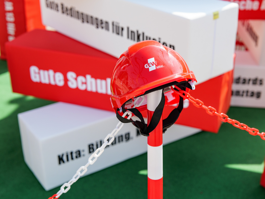Ein GEW NRW-Helm hängt auf einem Kettenpfosten zur Absperrung der Baustelle Bildung. 